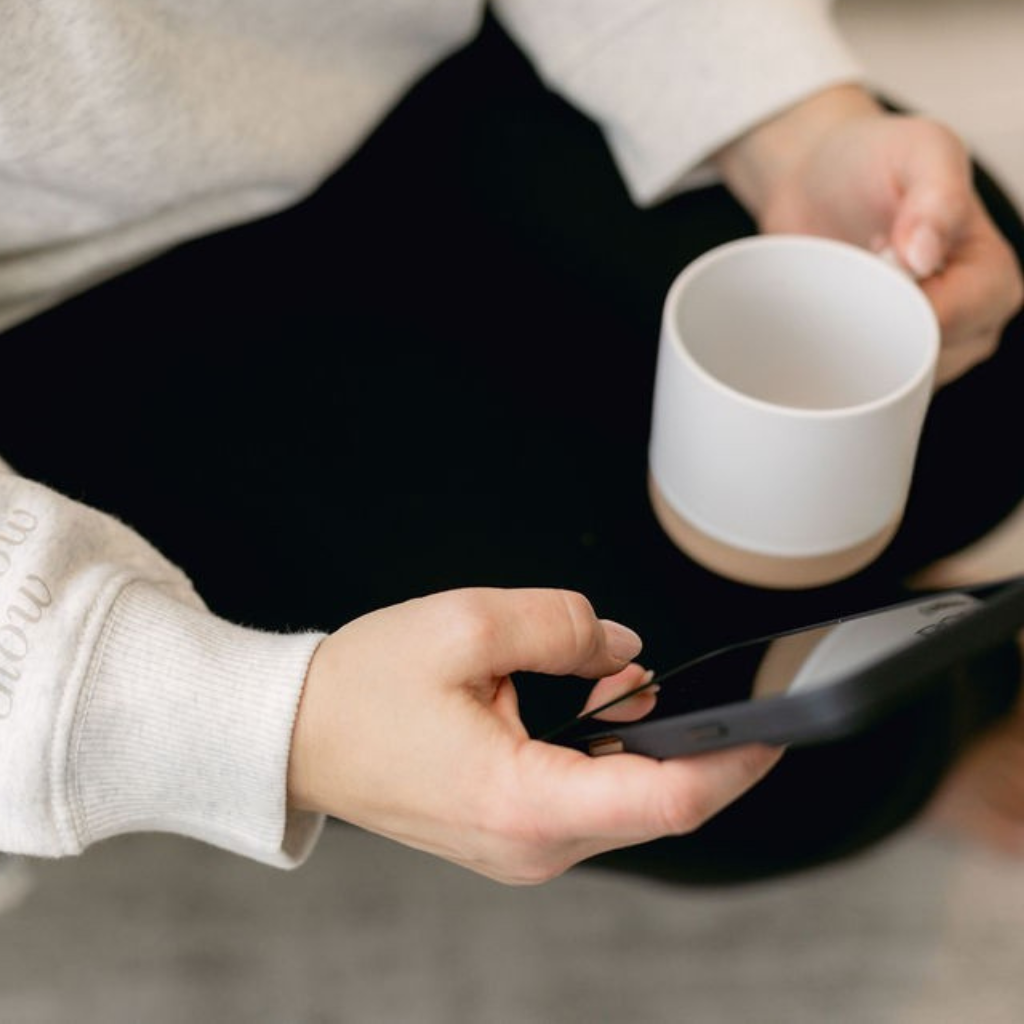 A client holding a phone showing a practice's branded Cadence rewards app, next to a coffee mug